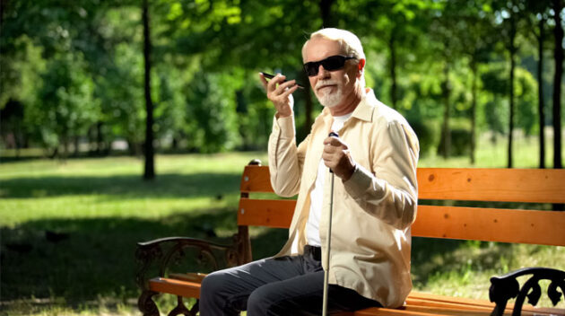 photograph-of-a-visually-impaired-elderly-person-sitting-on-a-park-bench-talking-on-the-phone